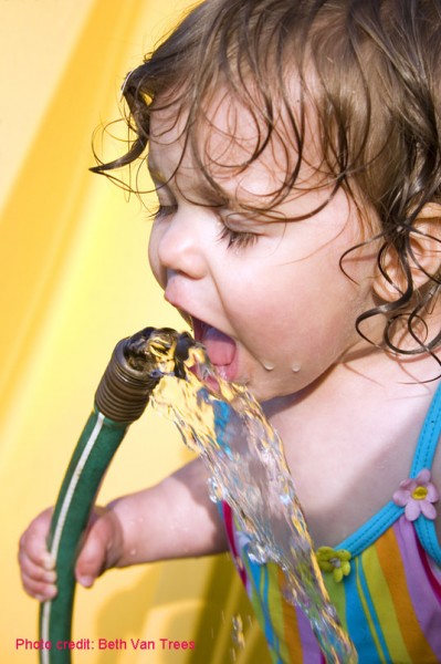 A toddler enjoys summer fun drinking from the garden hose